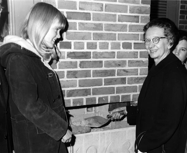 A woman and a student ceremonially install the building cornerstone.